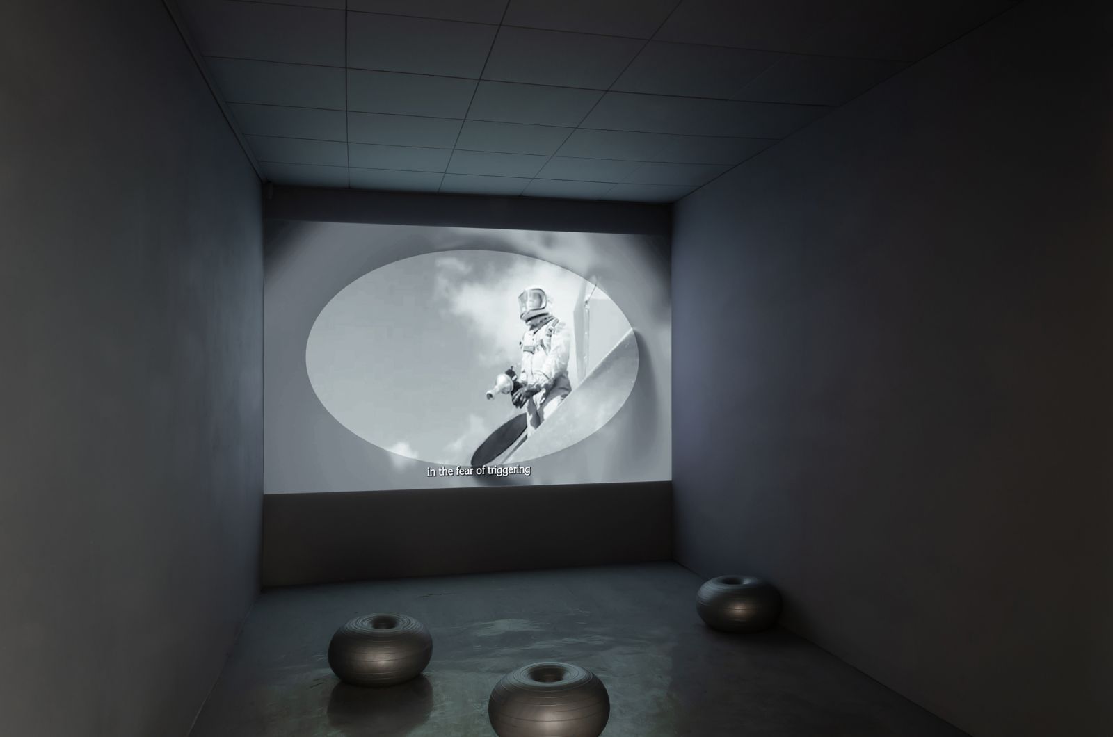a dark space with a projection and 3 donut-shaped seats, the subtitles on the projection say: 